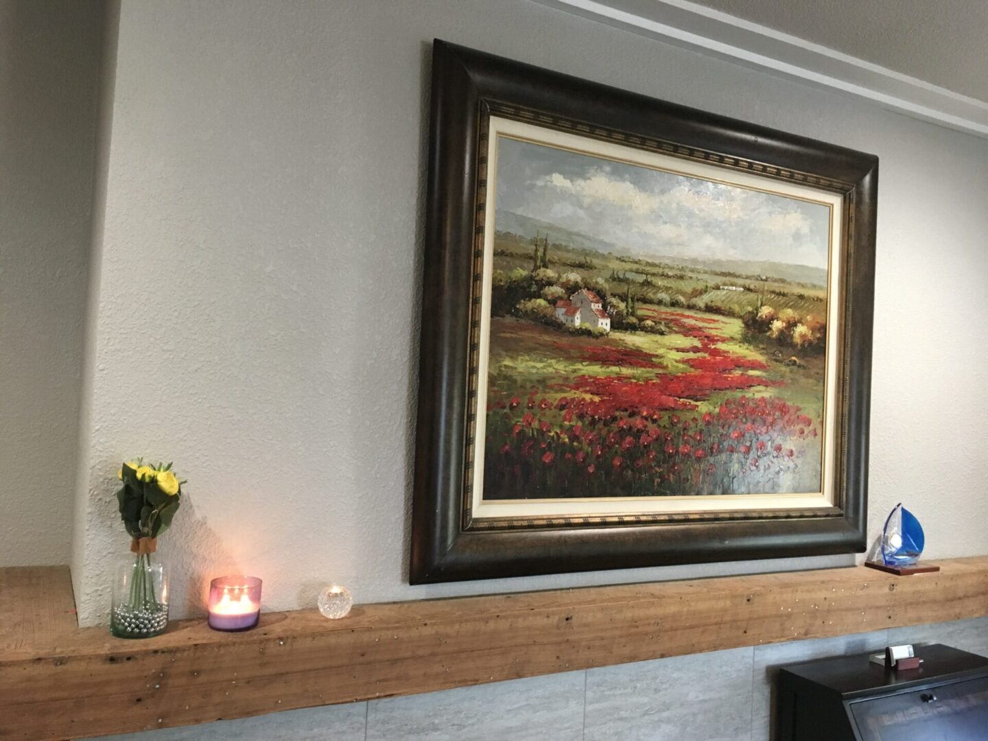 A painting of a field is on the wall above a fireplace.